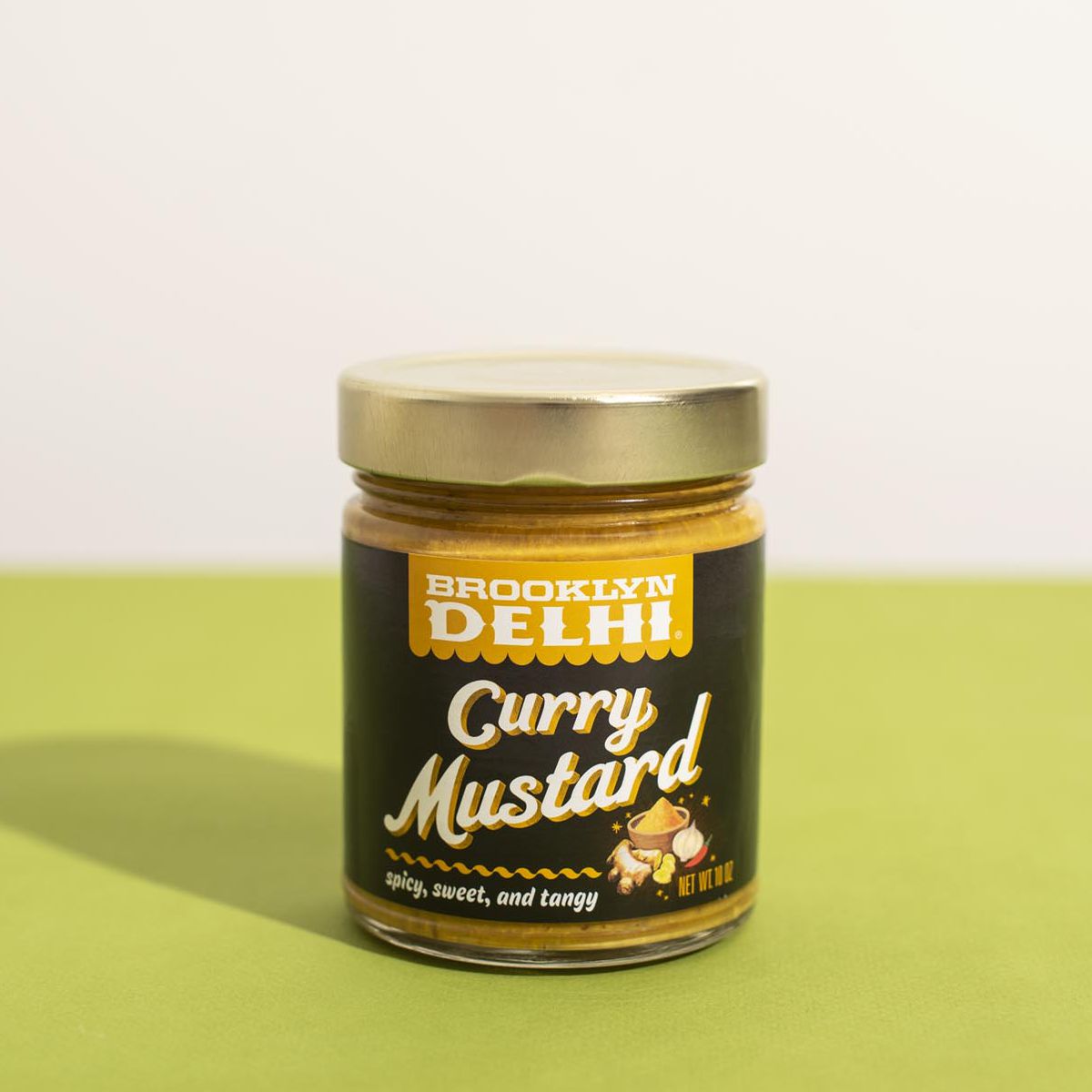 A jar of Brooklyn Delhi Curry Mustard on a green table.