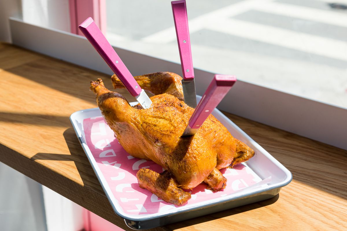 A roast chicken on a platter with three knives with hot pink handles stuck into it