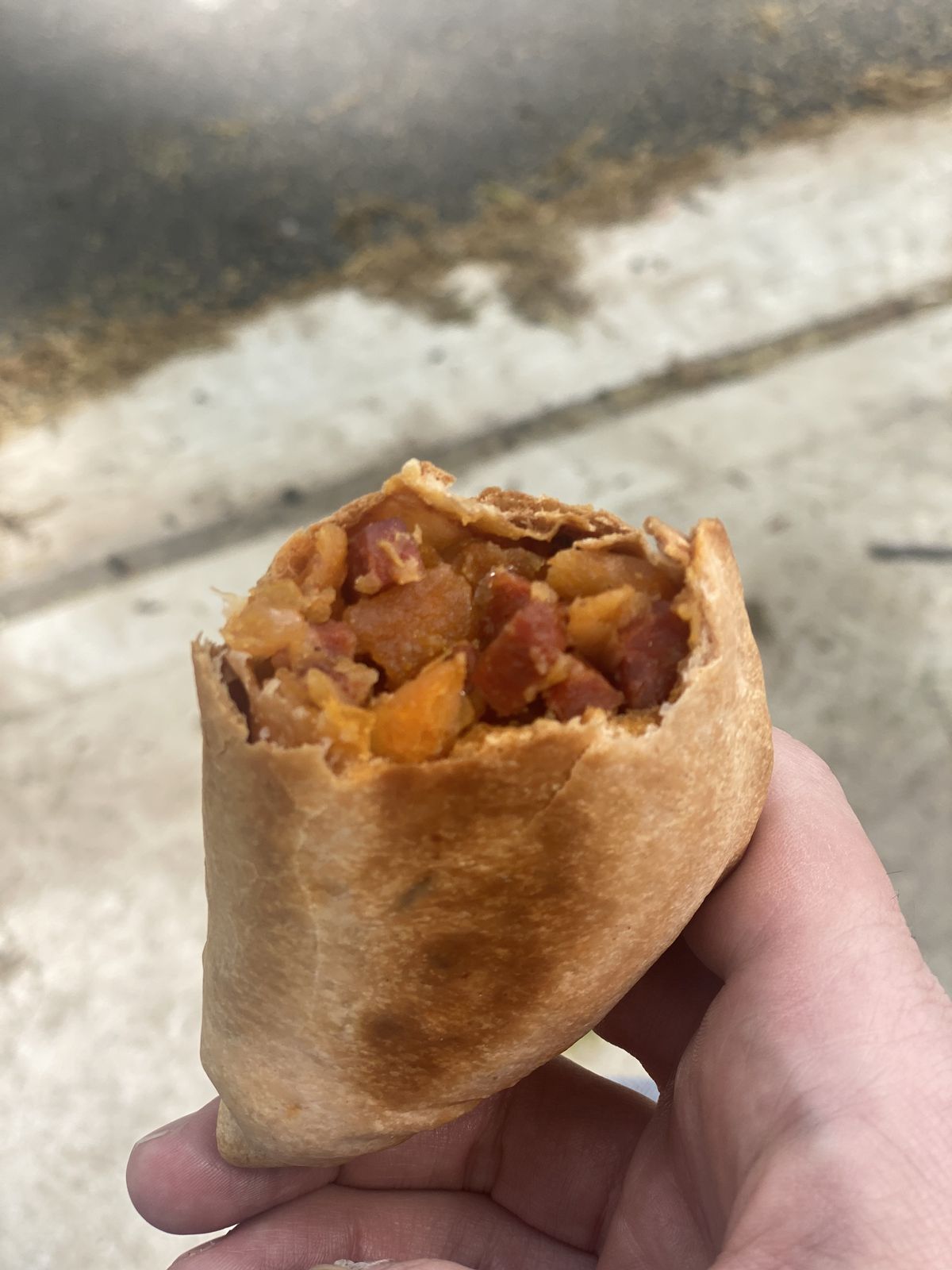 A customer holds a chorizo empanada upright; it’s filled with orange potatoes and red cubes of sausage