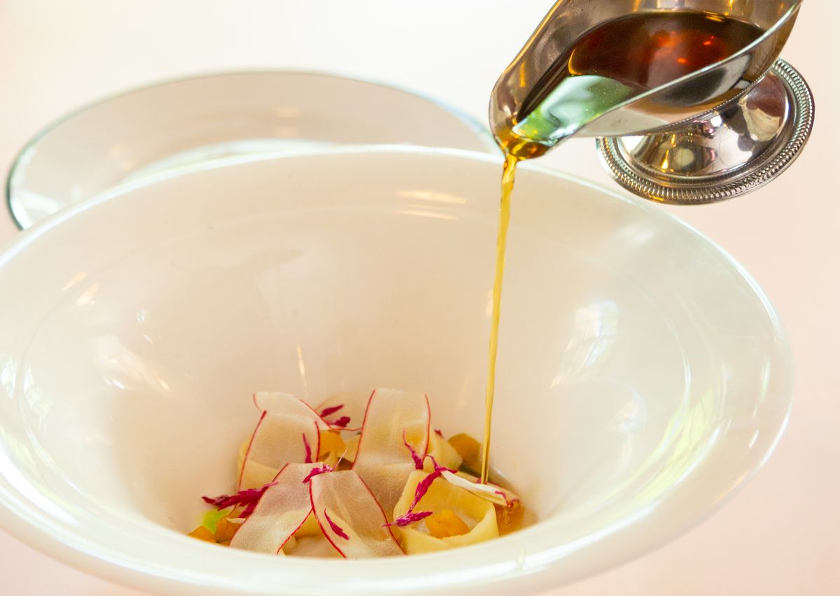 Duck consommé with foie gras dumplings, breakfast radishes, pickled apricot, and fine herbs served table side