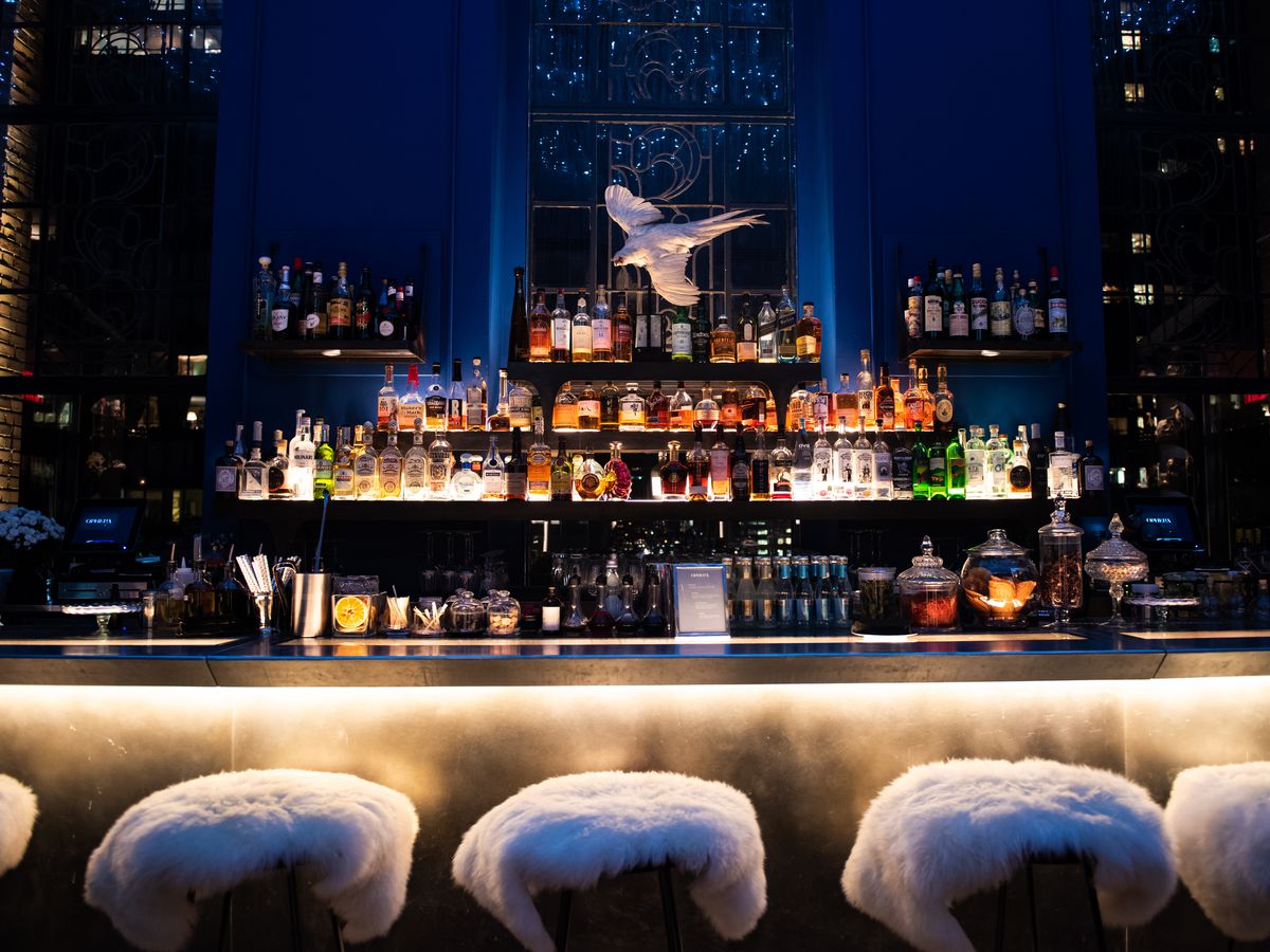 Sheepskin throws cover bar stools at an upscale bar with rows of bottles.