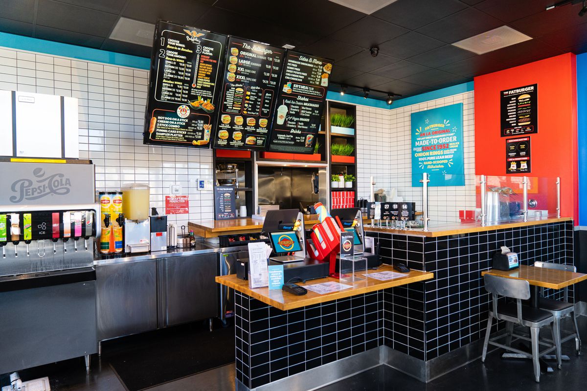 A corner ordering counter for a fast food restaurant, with menu hanging and black tile.
