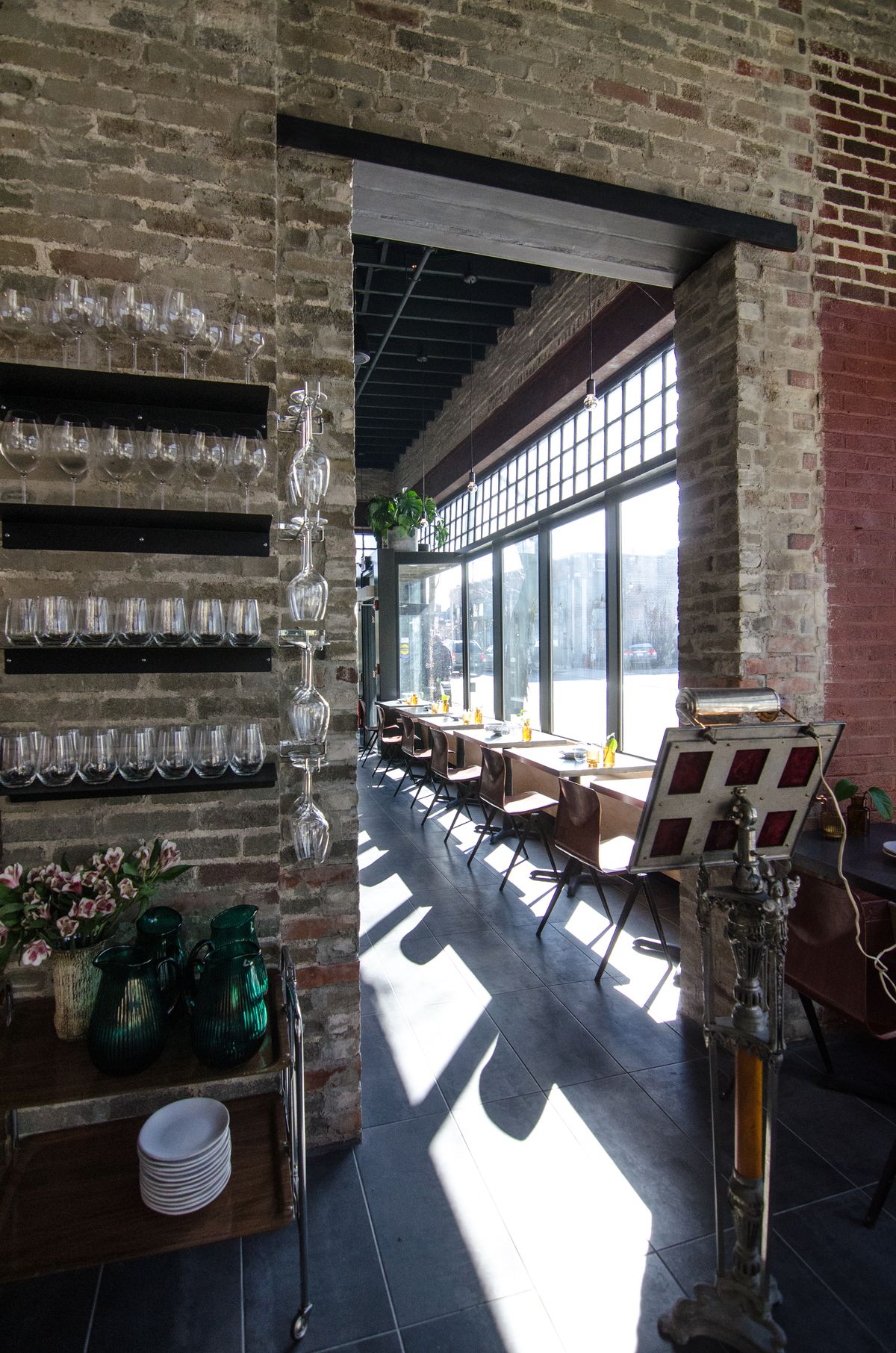 Restaurant interior features lots of exposed gray brick and natural light. An Art Deco-style podium sets off one dining area from another.