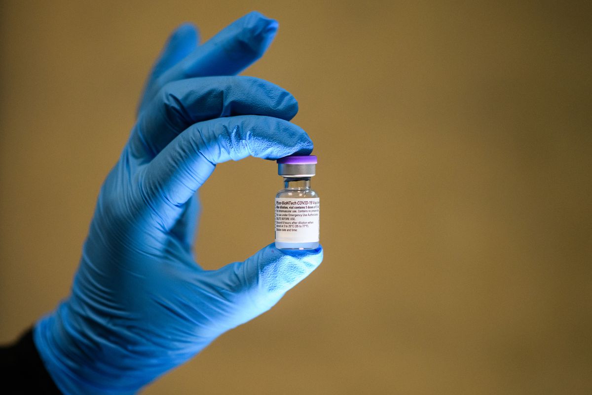 A vial of a Covid-19 vaccine held up by a blue-gloved hand.