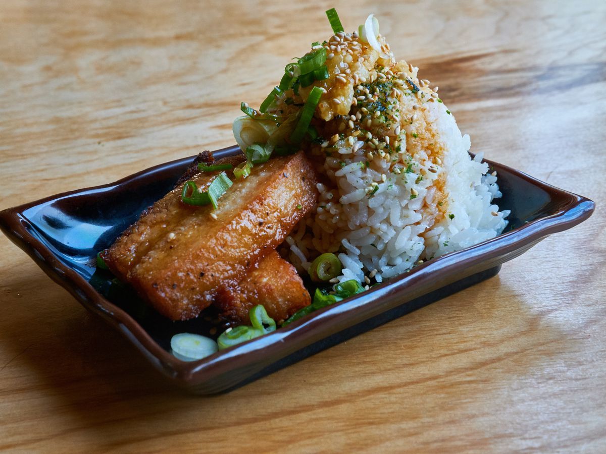 Fried pork belly and white rice, topped with soy sauce and scallions, on a dark ceramic plate.