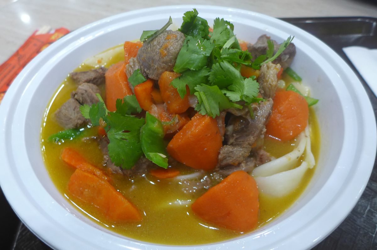 A bowl of soup with wide wheat noodles, lamb, and carrots.