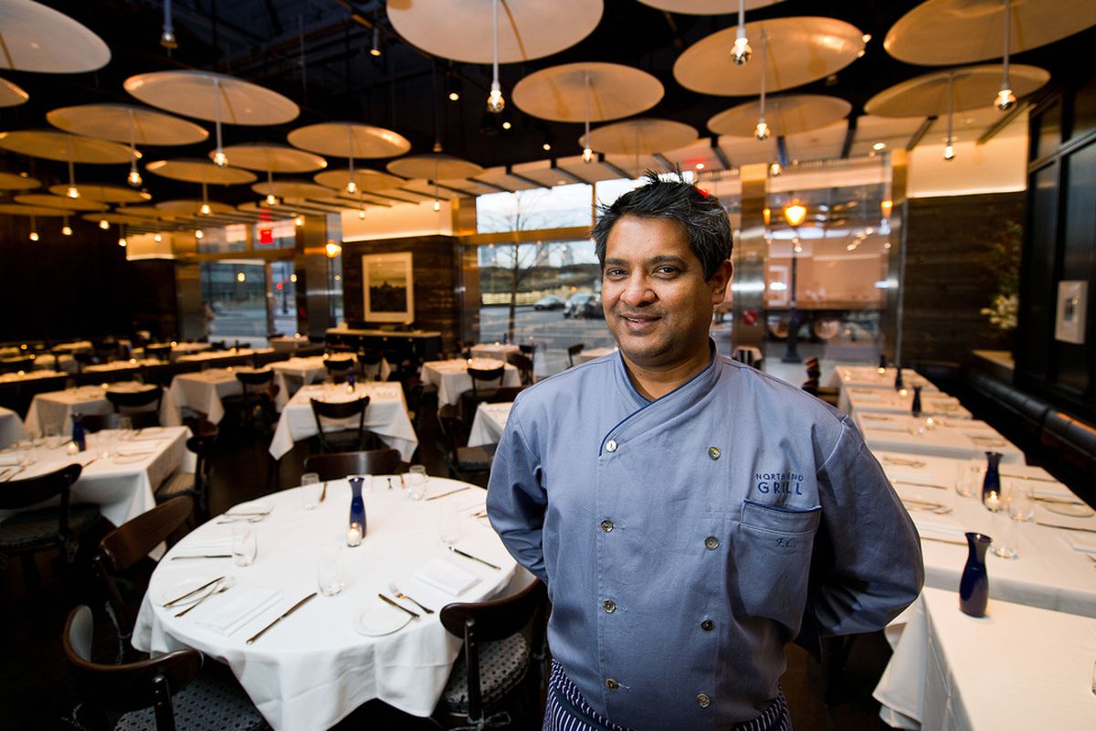 Floyd Cardoz, wearing a blue shirt, stands in an empty dining room.