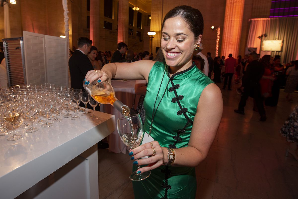 A woman in a green dress smiles as she pours wine from a bottle into a glass.