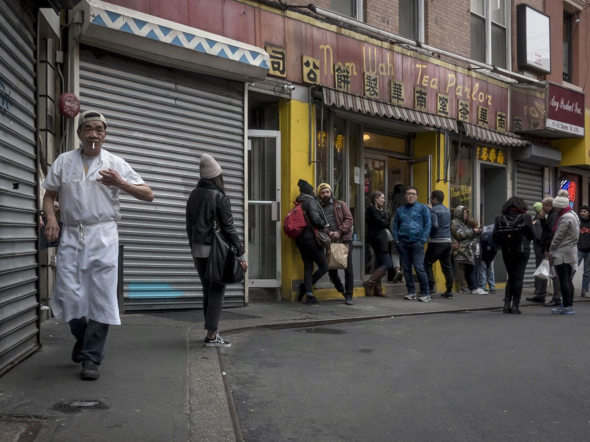 A chef hustles in the foreground as a knot of customers wait in the background on a darkened Doyers Alley.