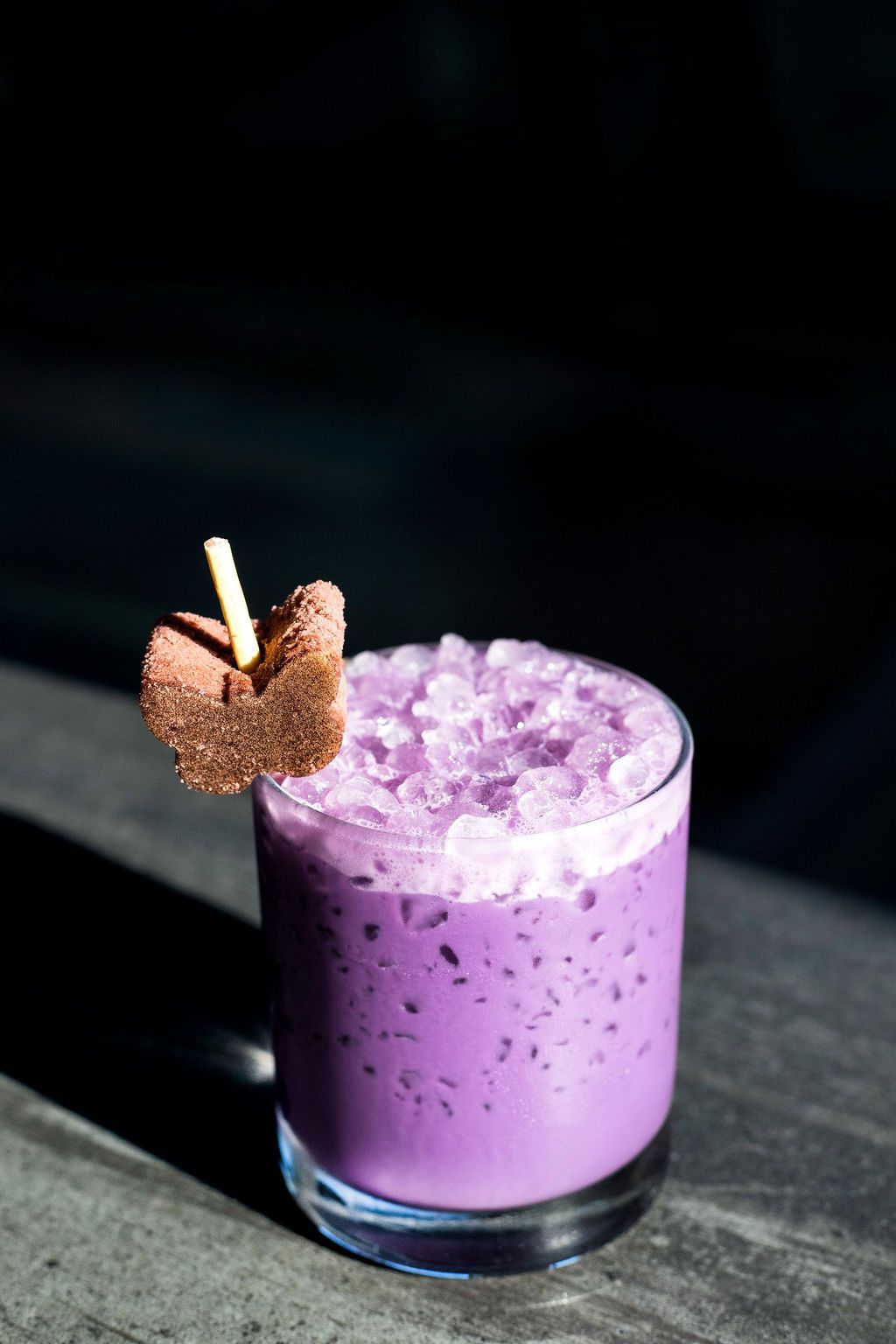 A glass filled crushed ice and a lavender ube-colored coctail, garnished with a butterfly-shaped sponge cake on a Pocky stick.