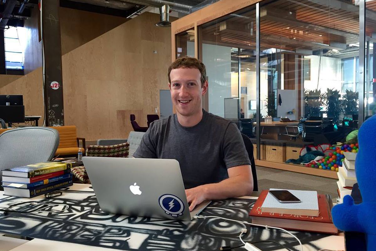 Facebook CEO Mark Zuckerberg sits at a table and ties on a laptop.