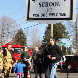 Parents walk past police and firefighters away from the Sandy Hook Elementary School with their children following a shooting at the school, Friday, Dec. 14, 2012 in Newtown, Conn. A man opened fire inside the Connecticut elementary school where his mother worked Friday, killing 26 people, including 20 children, and forcing students to cower in classrooms and then flee with the help of teachers and police. 