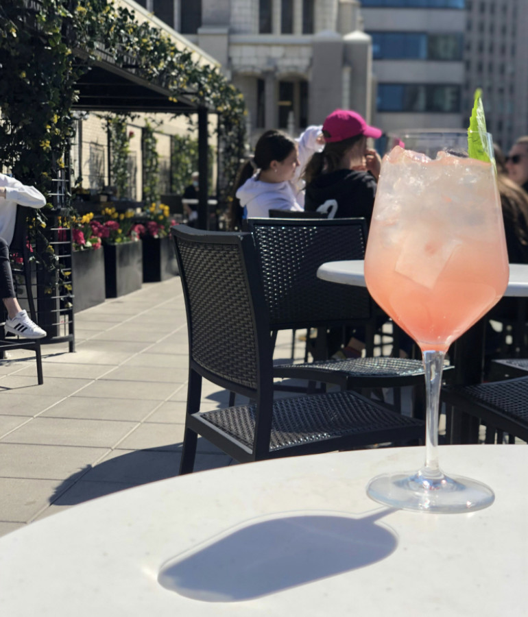 A pink Melon Spritz cocktail at London House sits in a large wine glass in their patio area