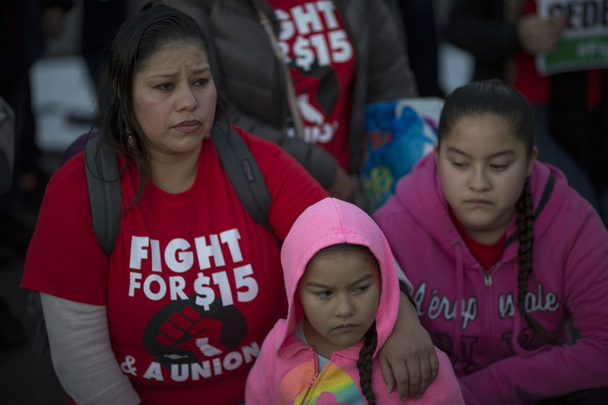 A protestor wears a shirt that reads “Fight for $15” while at a rally with her two daughters.