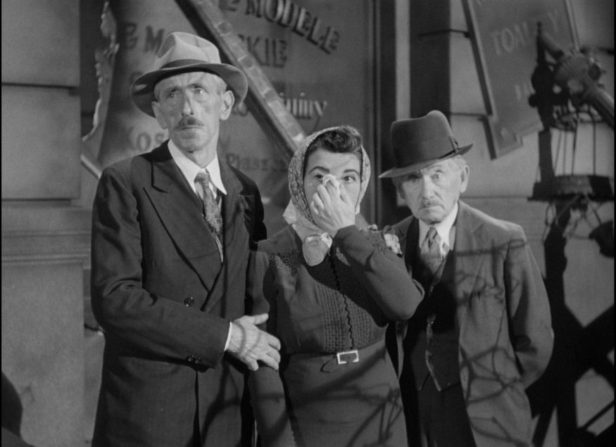 A group of people stand together, with one touching a tissue to their face, in Ernst Lubitsch’s To Be or Not to Be.
