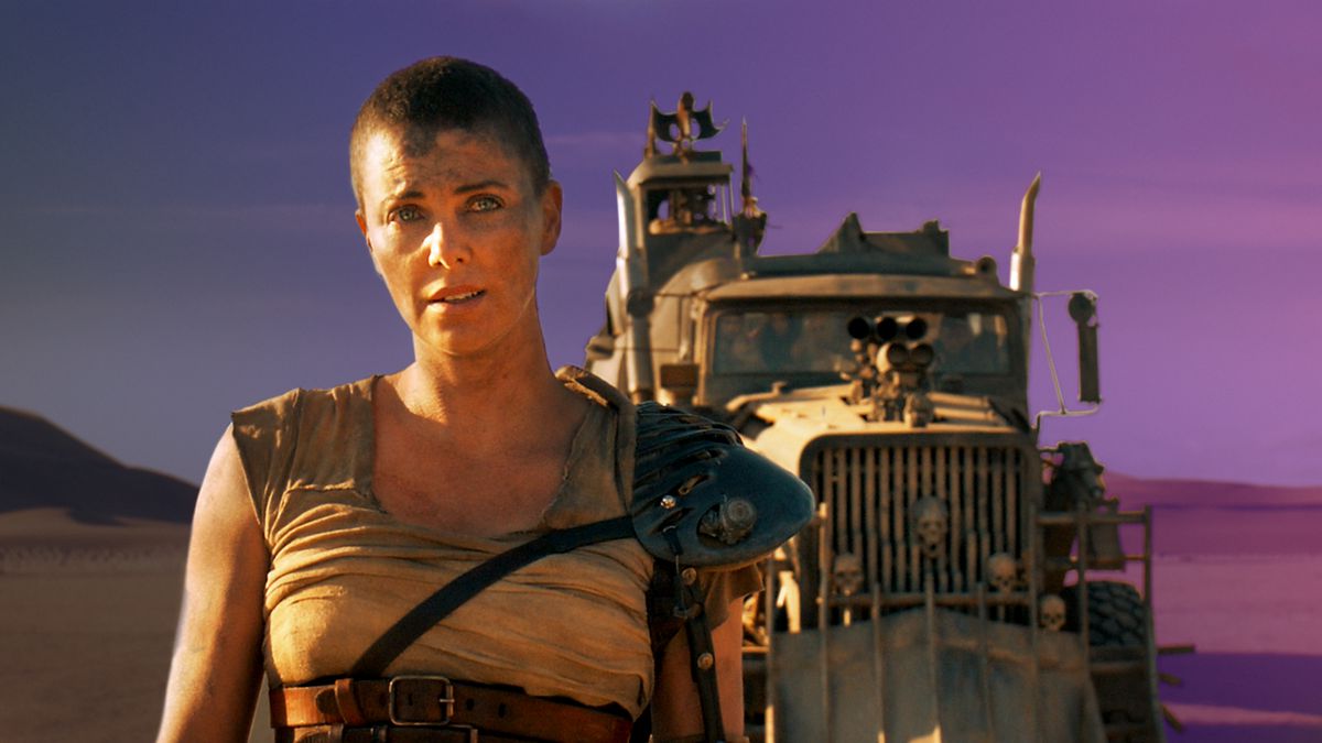 Charlize Theron stands in front of a post-apocalyptic truck in the movie Mad Max: Fury Road