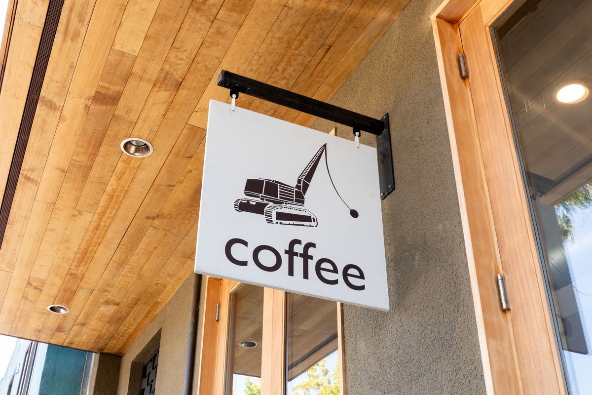 A white sign with a picture of black wrecking ball truck and the word coffee