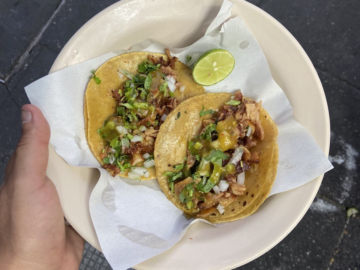 From above, two tacos on corn tortillas topped with tripas, onions, and salsa, on a plate held above the ground.