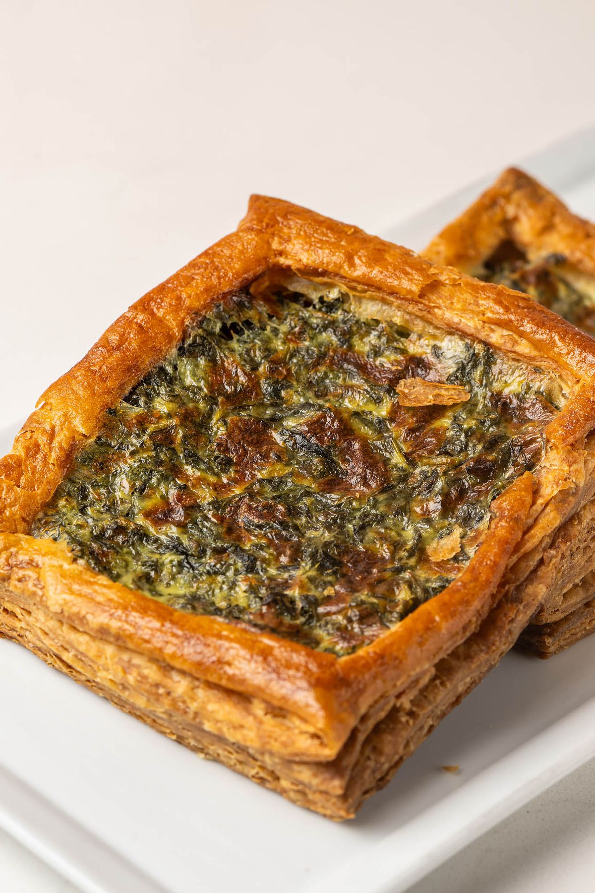 Greens cooked down inside of a wide, square pastry cooked to a dark brown on a white tray at an LA bakery.