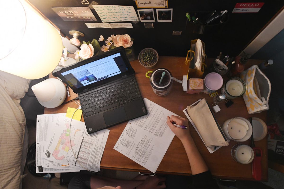 Bird’s-eye view of a high school student’s home desk with a laptop, coffee cup, and papers.