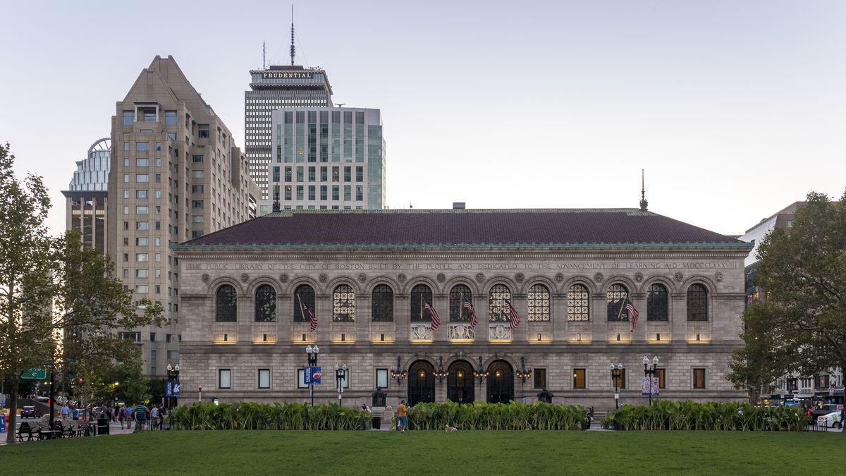 The exterior of the McKim building at the Boston Public Library. The building is large with many windows. There is a green lawn in front of the building.