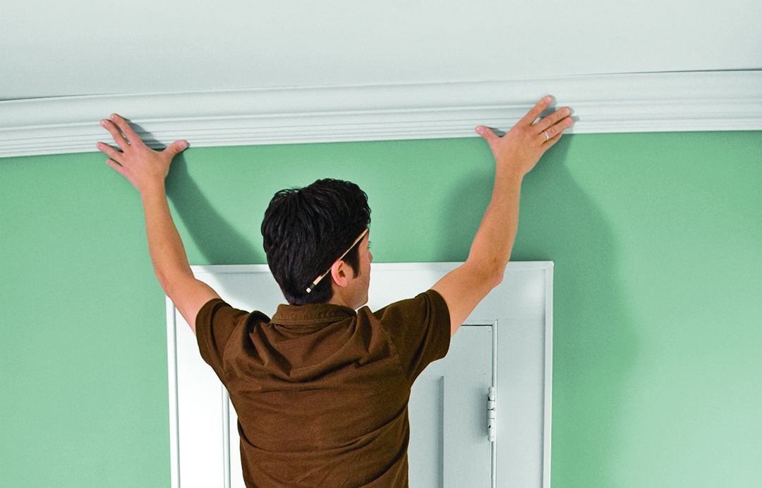 Man Holds Strip Of Molding Above Door