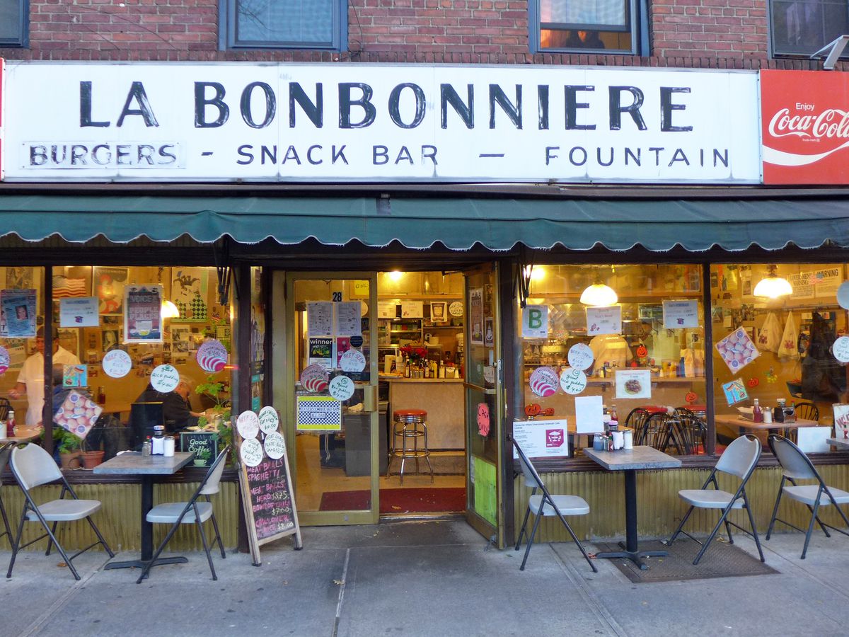 The exterior of La Bonbonniere, with tables and chairs and huge white sign bearing the name.