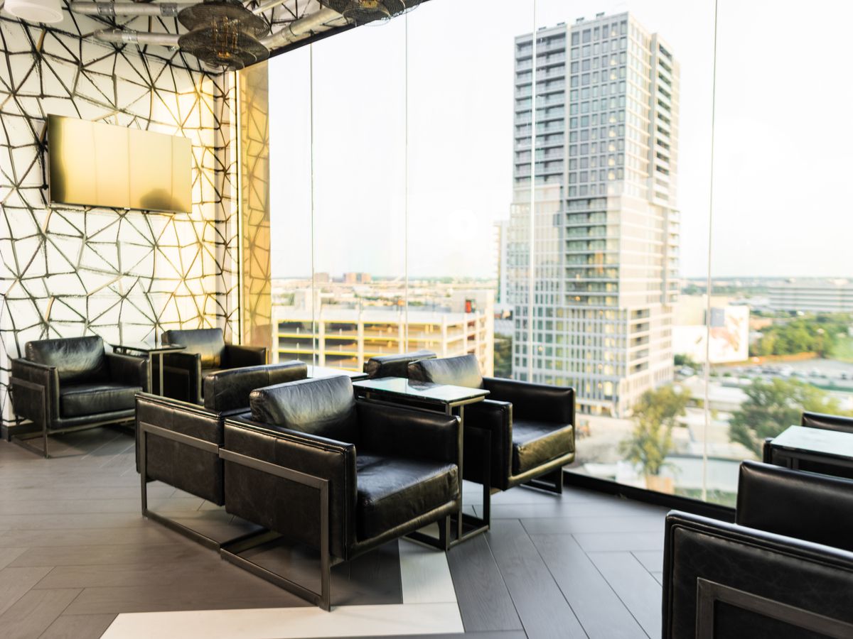 Leather club chairs sit in the foreground as a skyscraper rises in the background outside the window of Sky Blu Rooftop Bar.