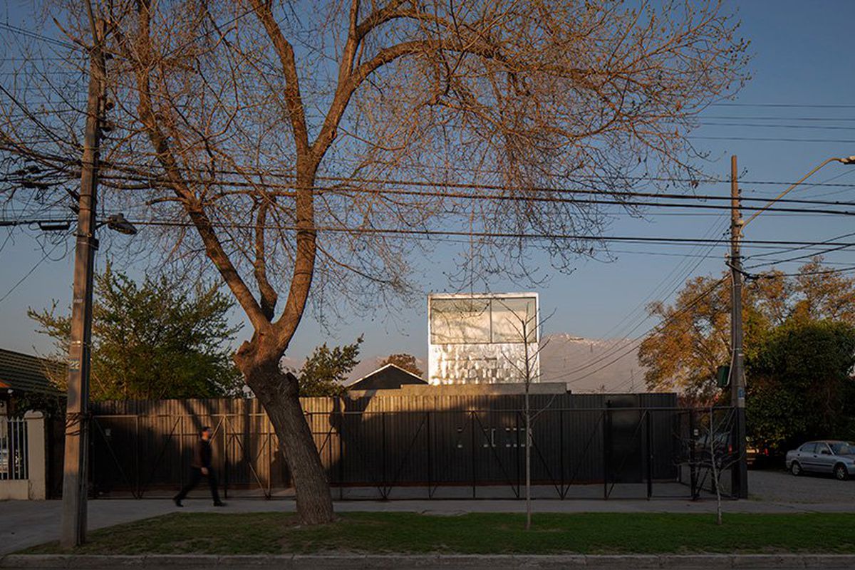 A rectangular metallic volume with a glass window rises above a fenced wall.