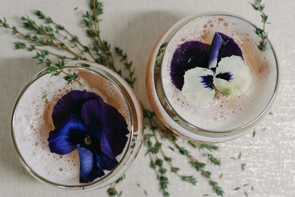Two cocktails shot from above called Peychaud’s Flowers garnished with edible violets. 