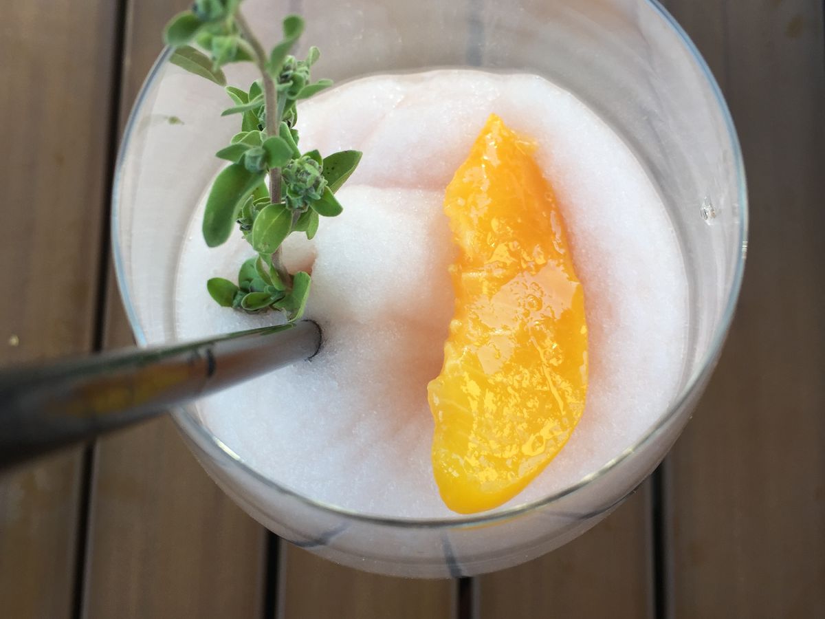 A white slushy cocktail topped with peach and herbs.