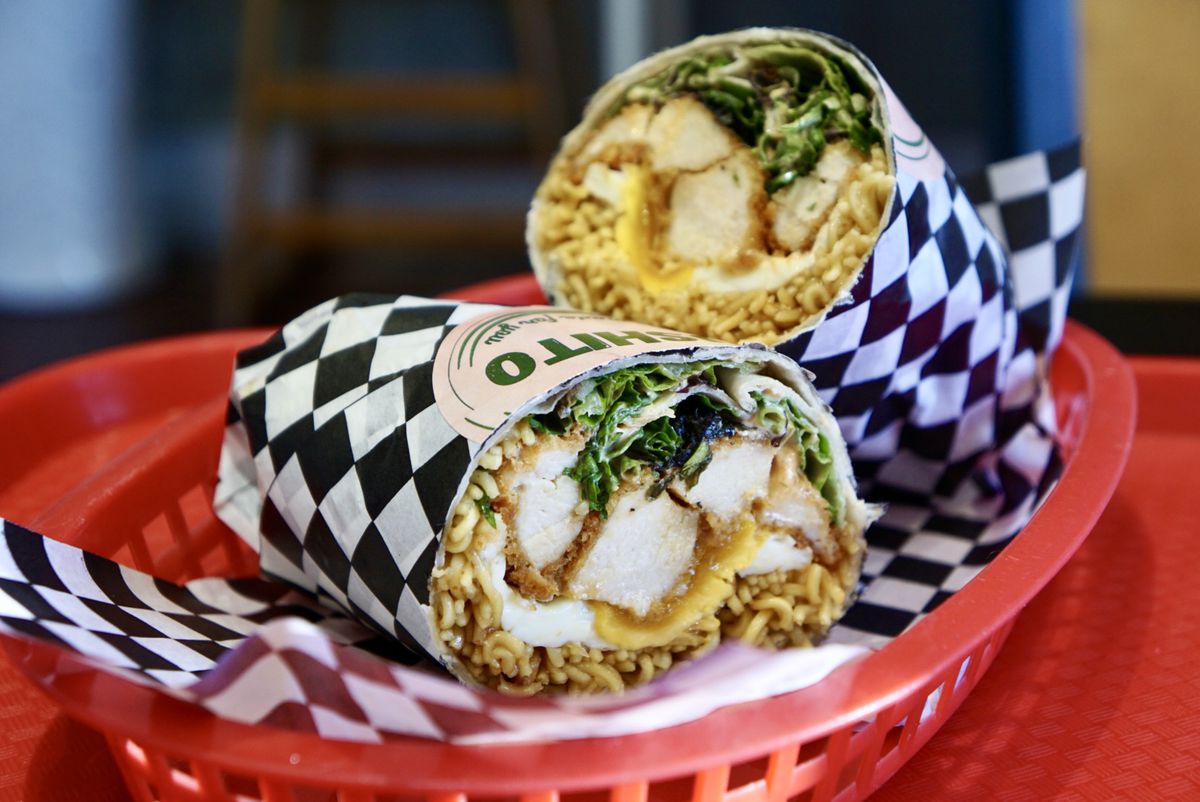 A katsu burrito wrapped in paper, placed into a red plastic basket