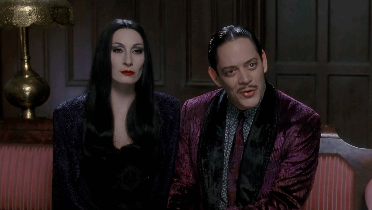 A pale, long-haired woman seated next to a man with slick black hair and pencil moustache clad in a velvet suit coat and tie.