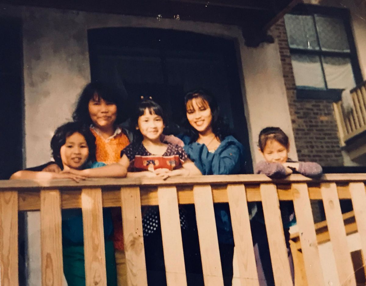 A group of five girls and women smile and pose as they look over a wooden balcony.