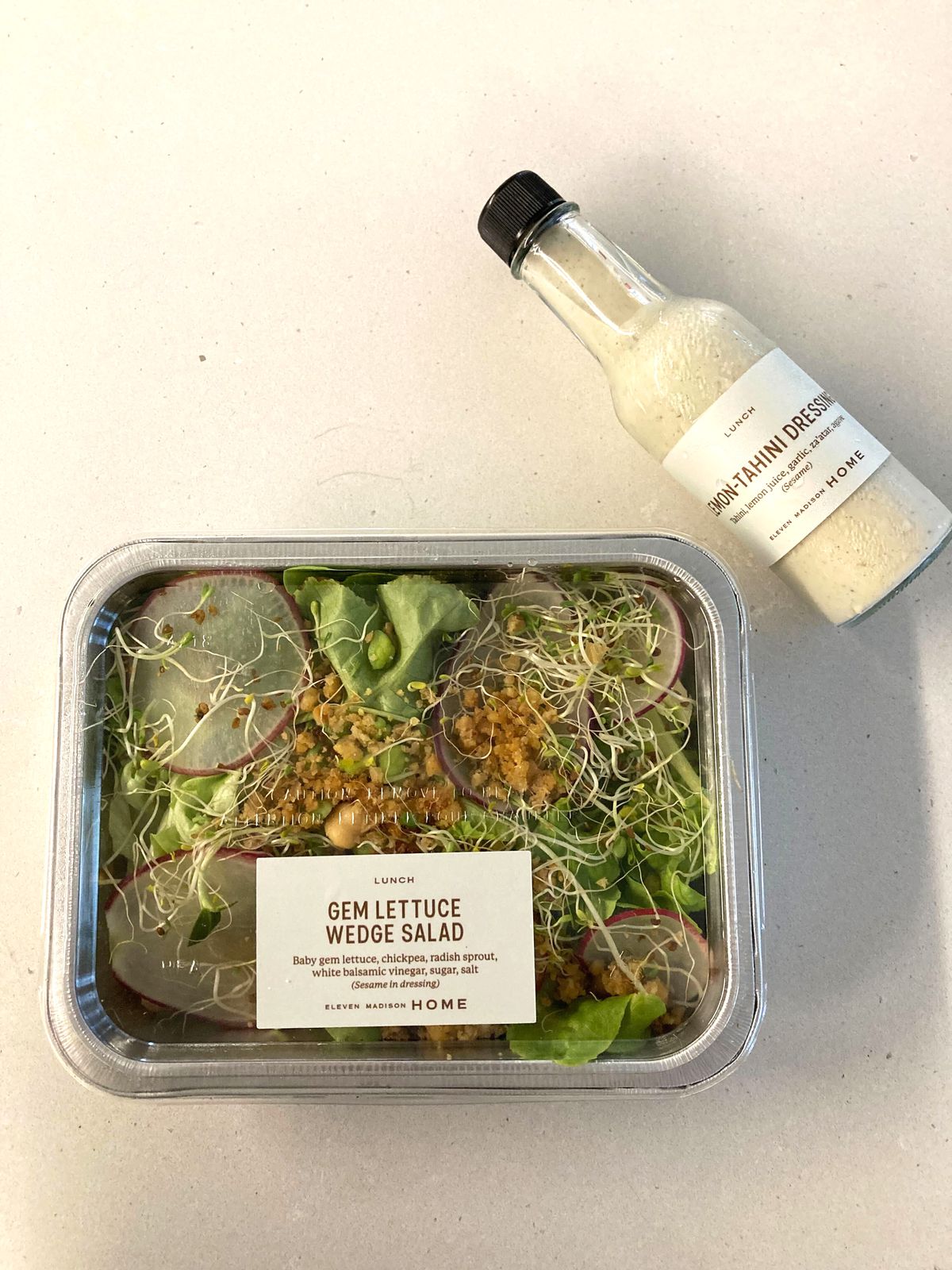 Salad in an aluminum takeout container next to a small bottle of salad dressing.