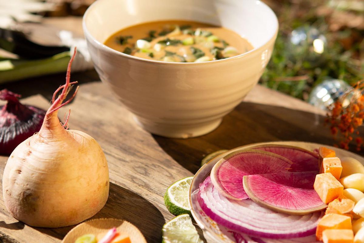 A bowl of Nourish Botanica Atlanta’s Carib coconut curry soup beside a whole turnip and slices of pink watermelon radish.
