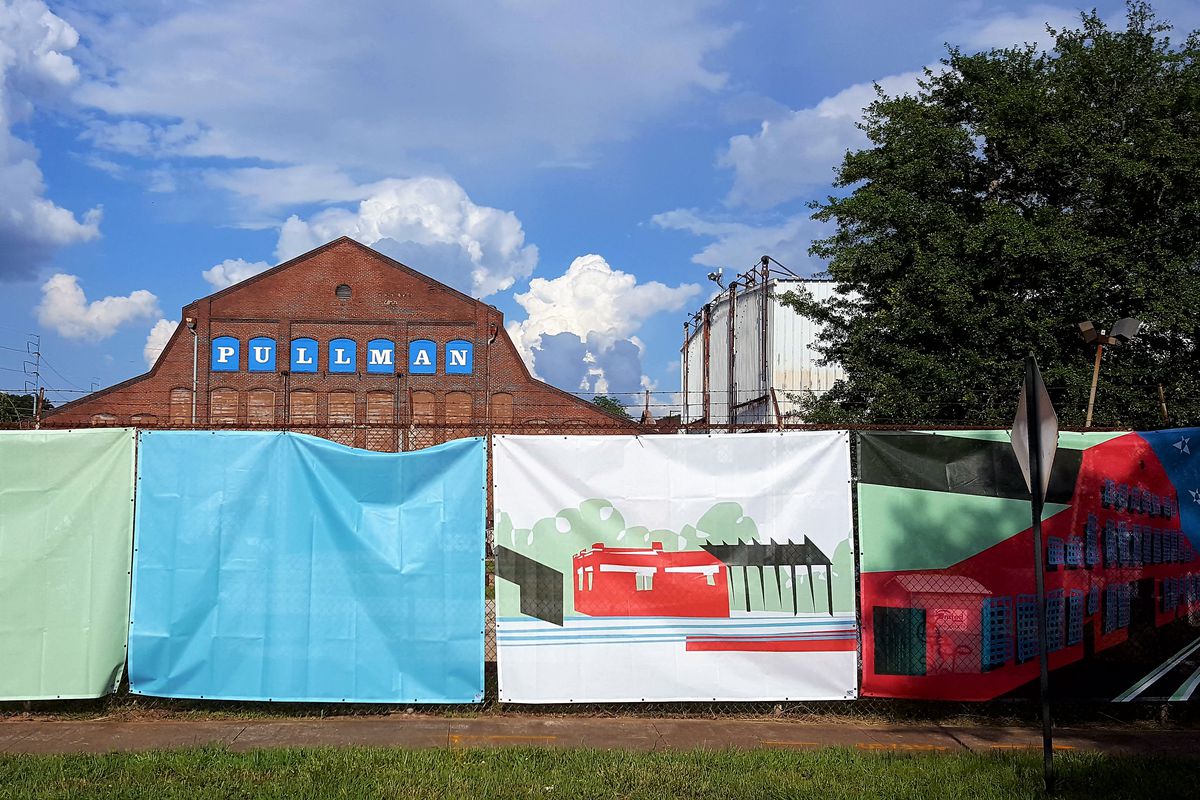 A colorful construction fence stands before an aging brick building adorned with the word “Pullman.”