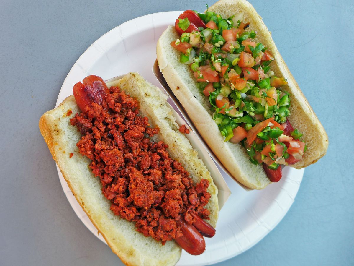 Two hot dogs, one topped with bright red ground meat, the other with a relish of chopped tomatoes and other vegetables.