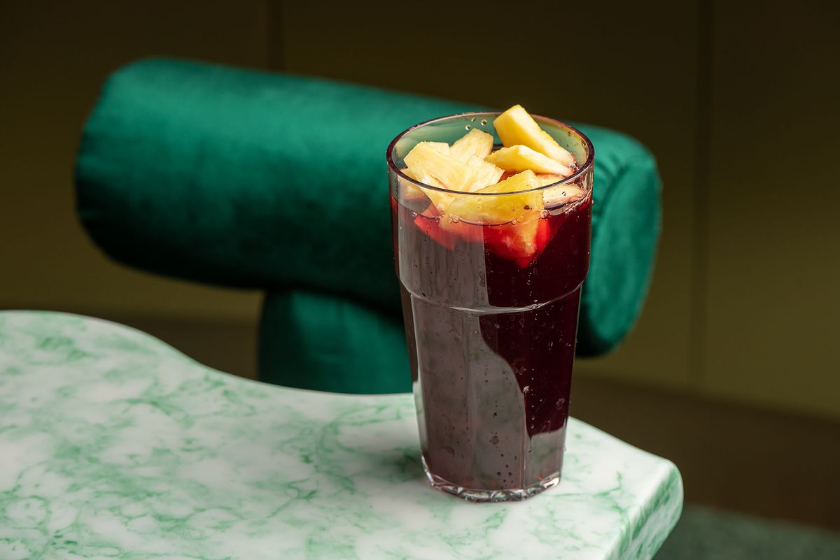 A tall glass filled with a dark purple beverage topped with fresh pineapple.