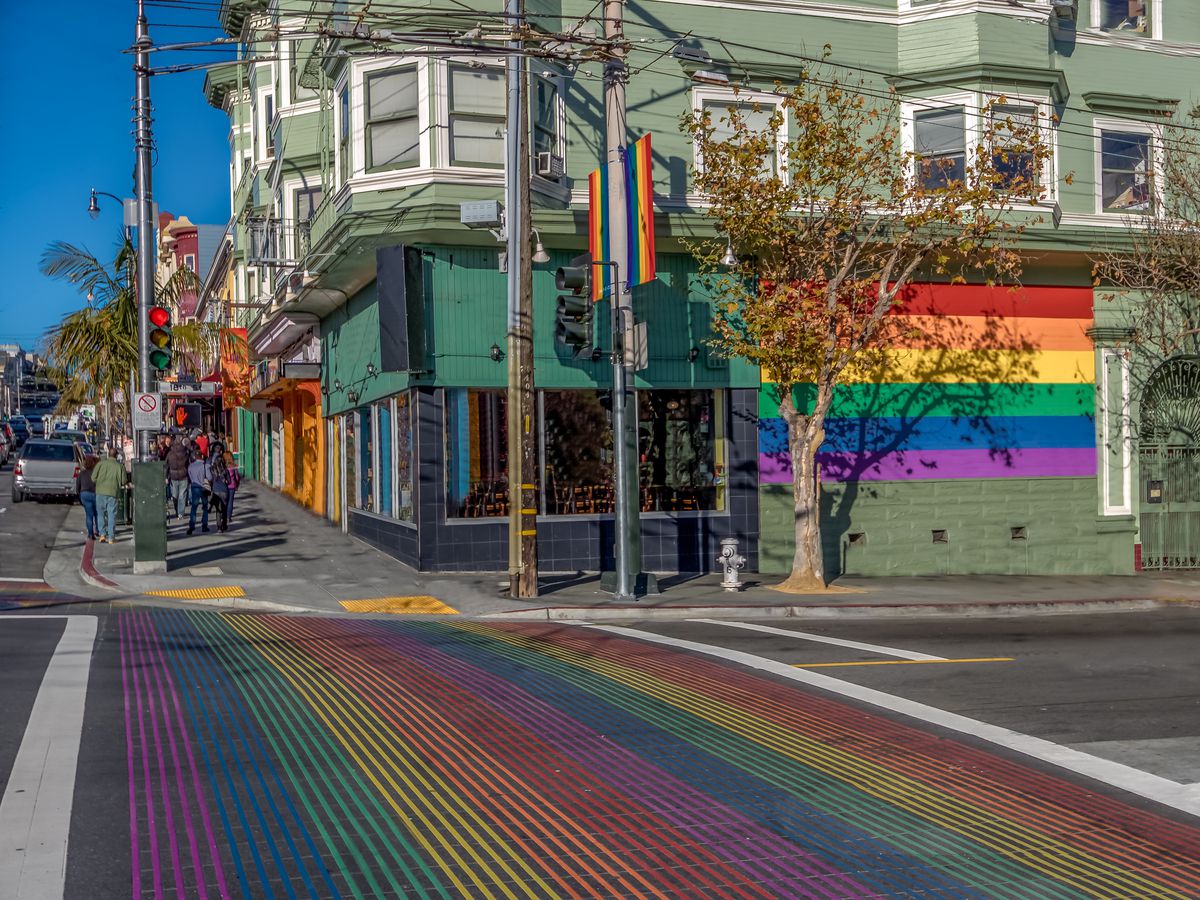 Rainbow crosswalk on Castro Street, rainbow flag on side of building.