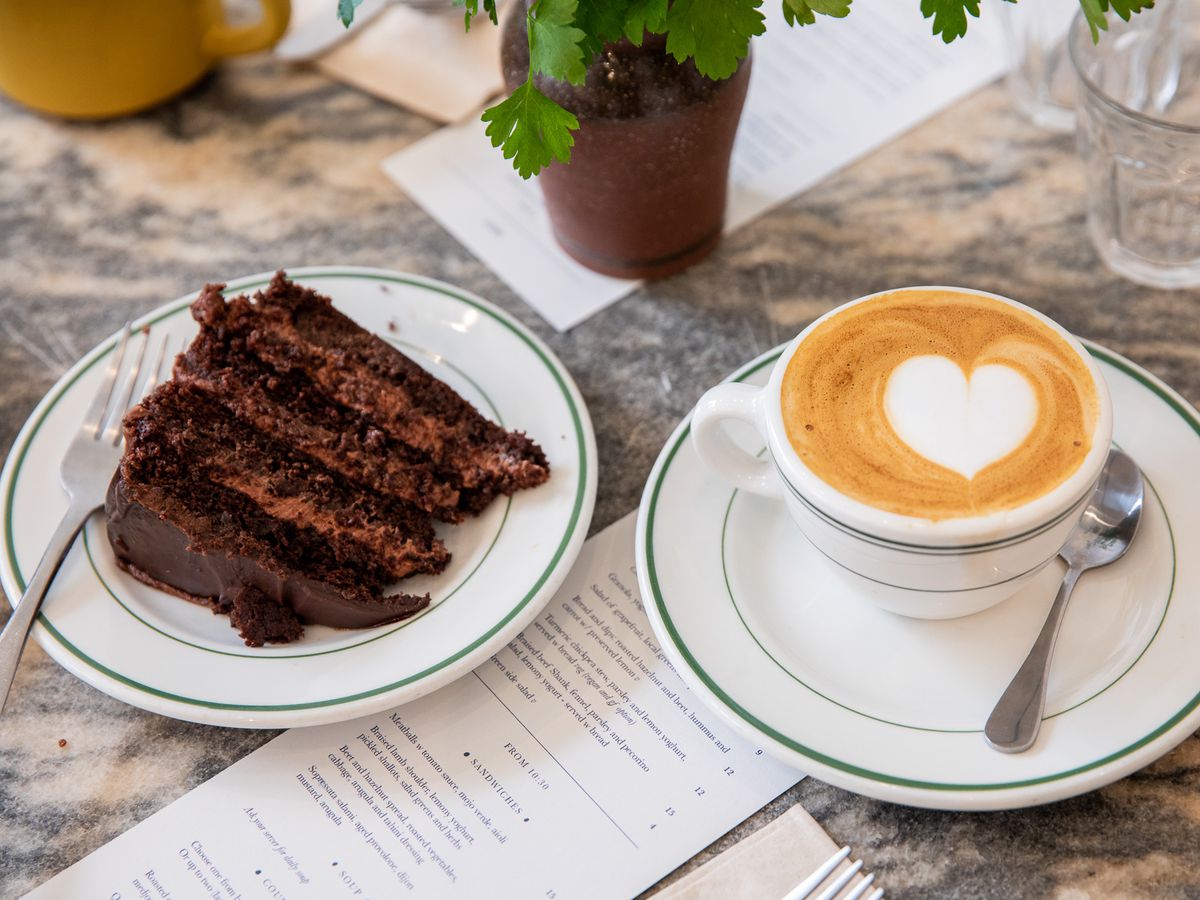 A slice of chocolate cake and a latte sit on plates at Ochre Bakery.