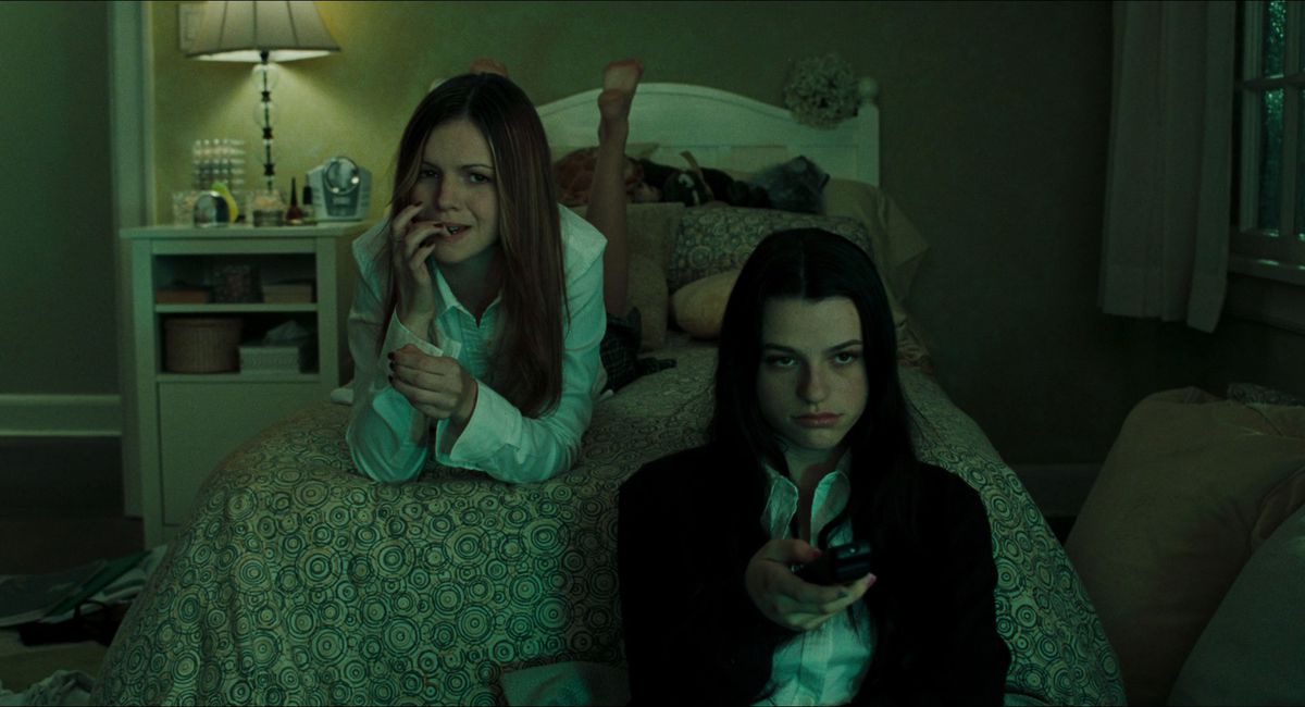 Teens Katie (Amber Tamblyn) and Becca (Rachael Bella) watch television on Katie’s bed in a screenshot from The Ring