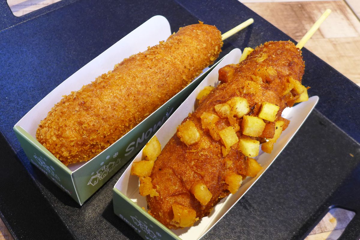Two corn dogs, sticks protruding, one with potato cubes on the outside, the other without.