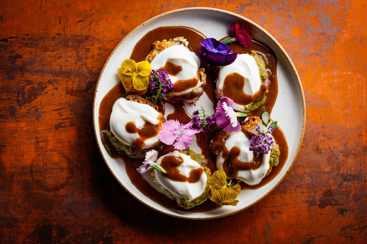 A plate of yogurt-topped patties decorated with edible flowers.