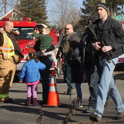 A law enforcement official carries a weapon as he walks past firefighters and parents with their children after a shooting at the Sandy Hook Elementary School in Newtown, Conn. on Friday, Dec. 14, 2012. 