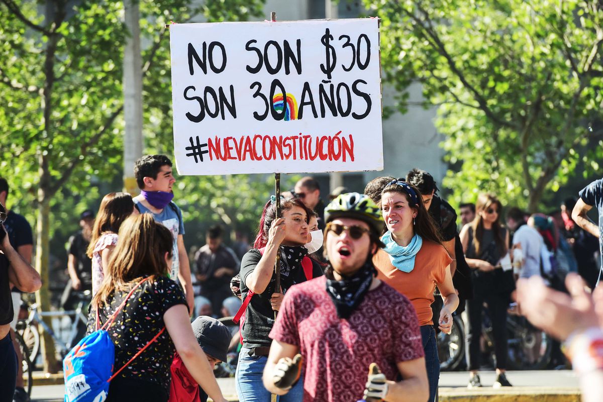 A protester in Chile holds a sign reading, “No son $30, son 30 anos #nuevaconstitucion.”