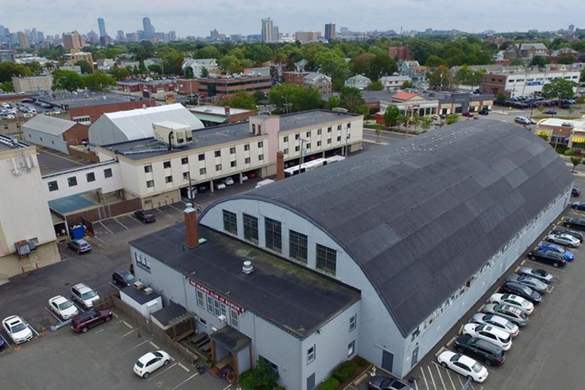 Aerial shot of a long building surrounded by parking, and the roof of the building is barrel-shaped.