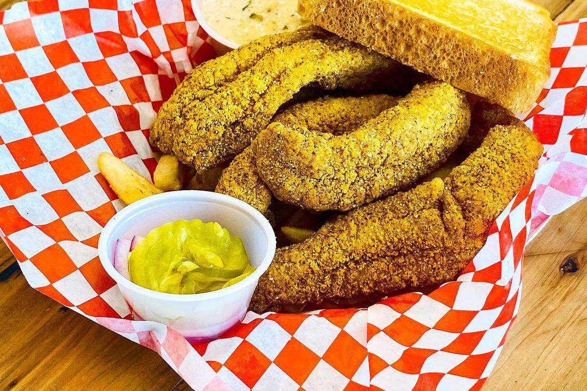 fried catfish tenders with thick toast, pickles, fries and tarter sauce in a plastic basket lines with red and white checkered paper