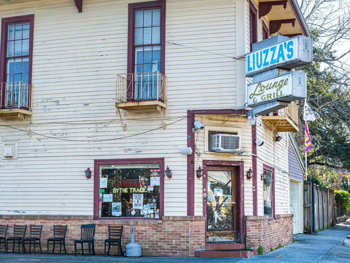 A corner no-frills building with light yellow siding, doorfront, and old Liuzza’s by the Track sign above.