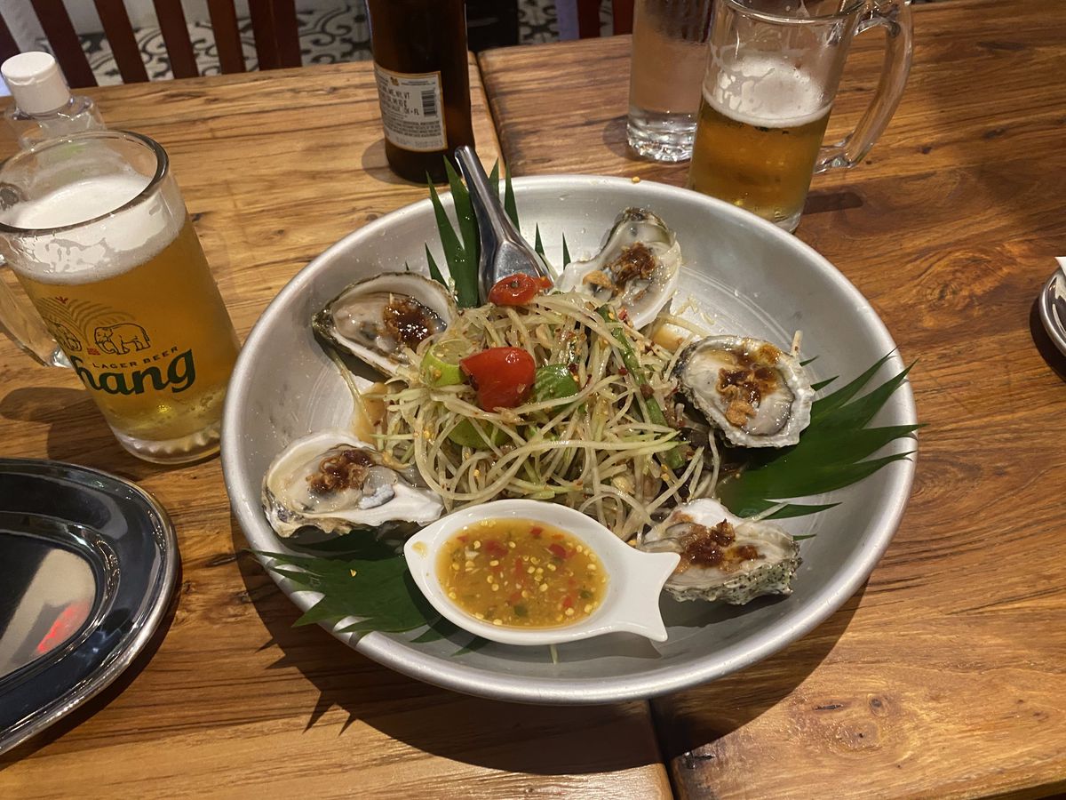 A stainless steel tray with papaya salad and a handful of oysters.